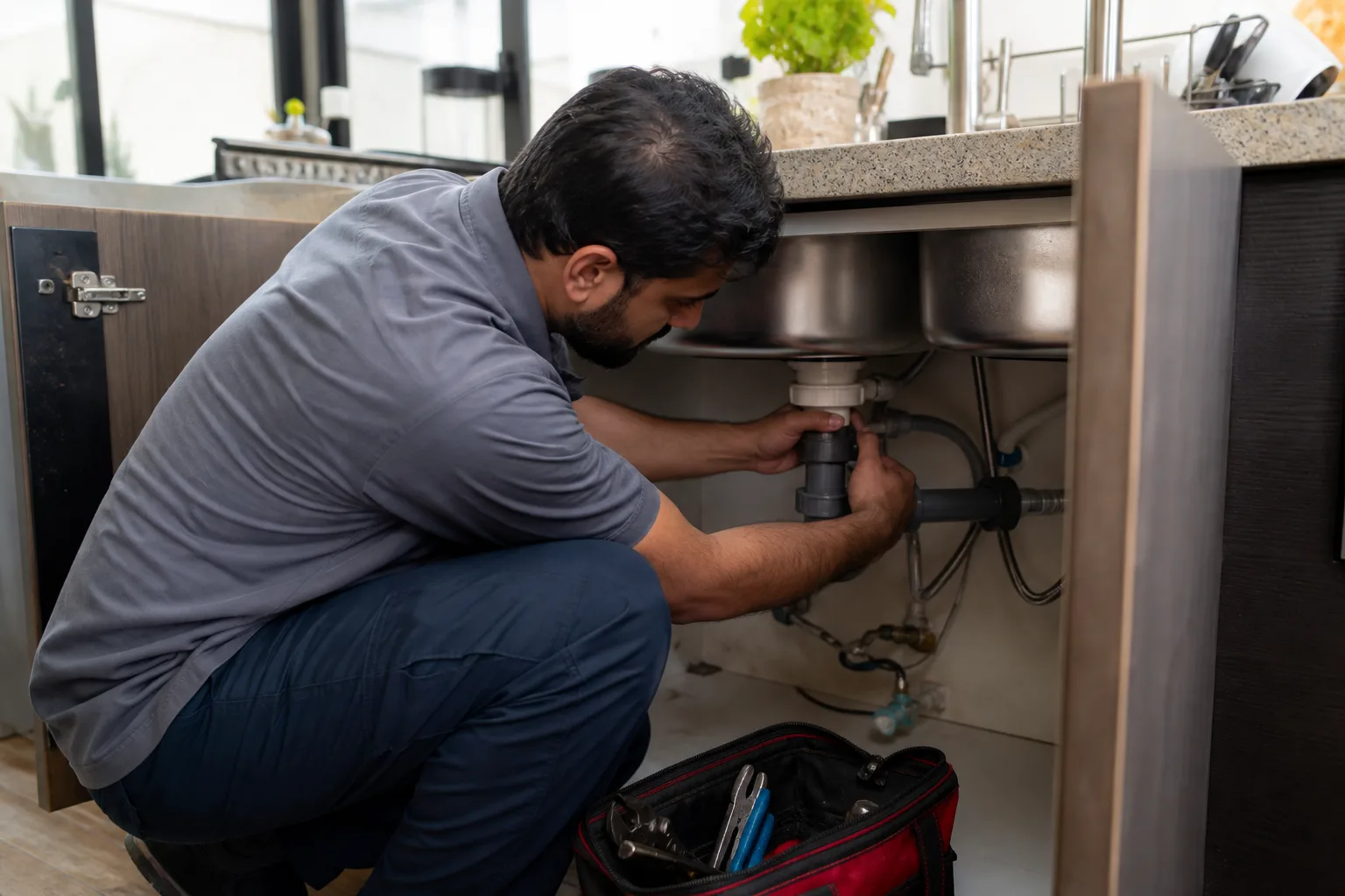 A professional repairing plumbing beneath a kitchen sink